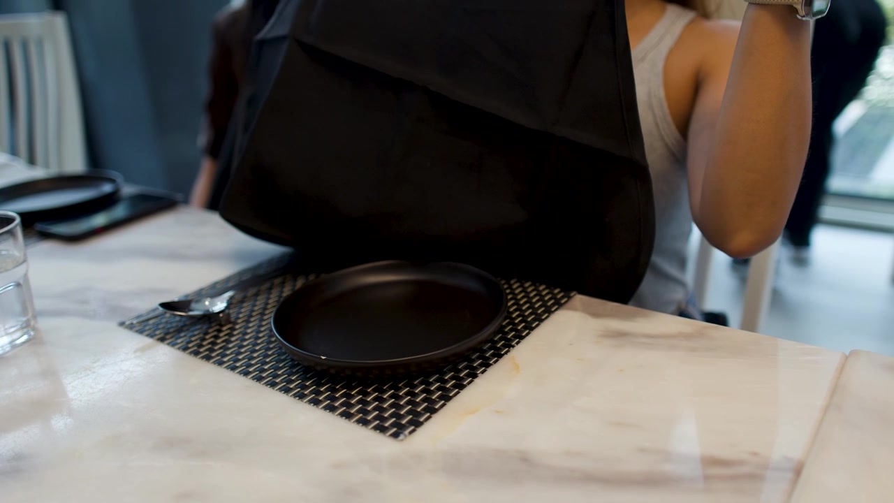 A woman prepares for a meal by putting on a black apron at a restaurant