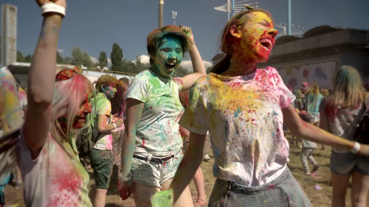 Three young multi-ethnic girlfriends are jumping and dancing with colorful powder on on holi festival in daytime in summer, friendship concept, color concept