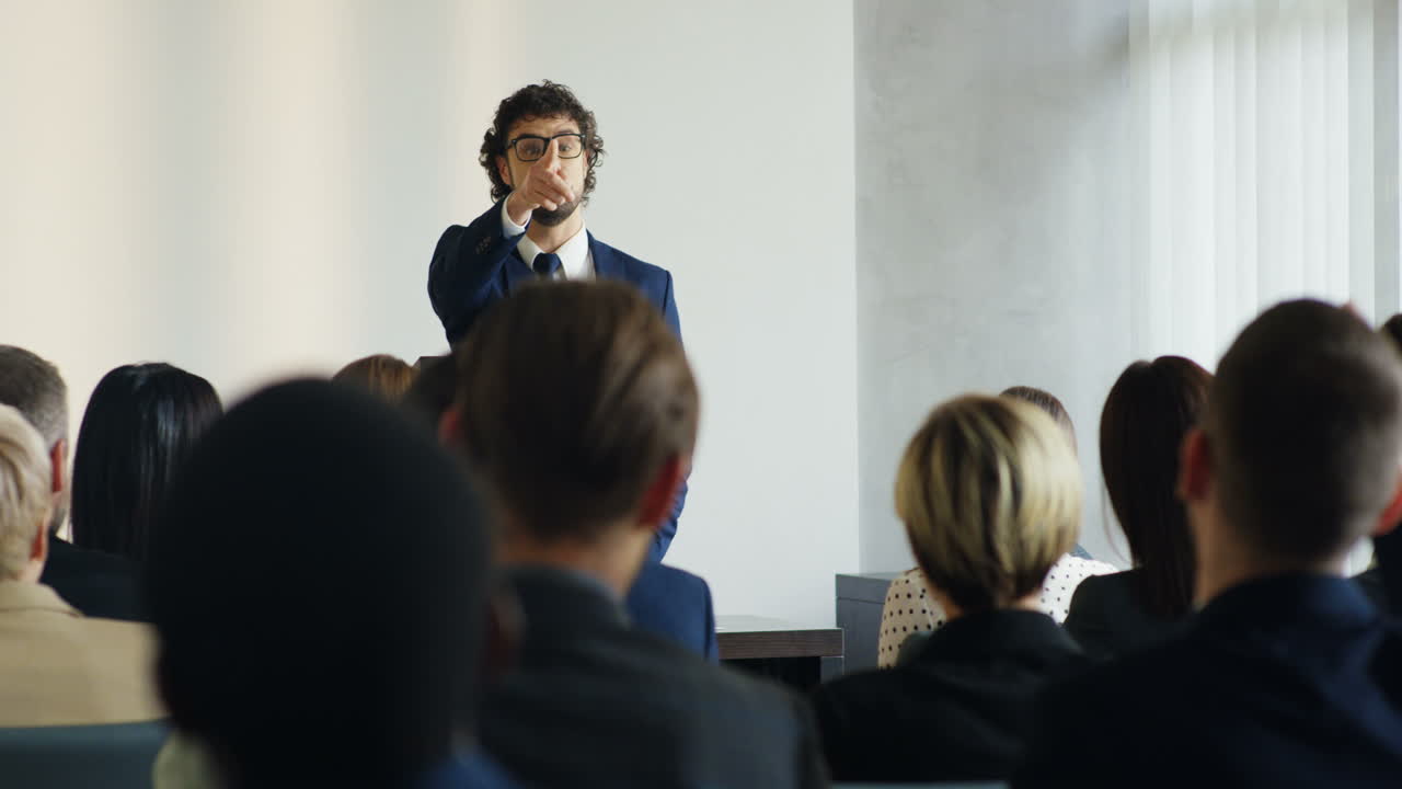 Caucasian businessman wearing glasses and formal clothes speaking at a conference in front of many people