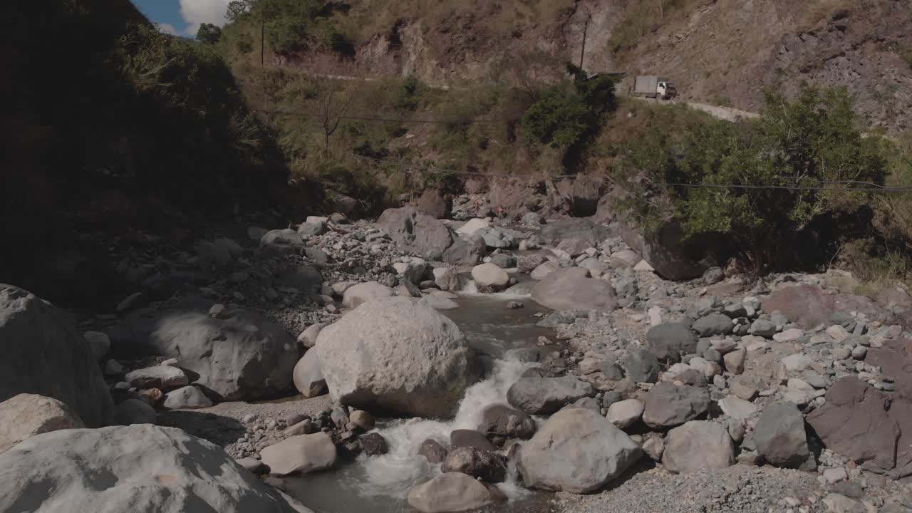 hermoso río rocoso que serpentea a través de las montañas en el valle del cañón agua que fluye acercándose cantos rodados grises árboles verdes cielo azul lento aéreo movimiento suave enfoque sobre el arroyo en cascada naturaleza
