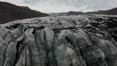 drone shot capturing the jagged ice formations and deep crevasses on the surface of sólheimajökull glacier in iceland, highlighting the rugged icy landscape