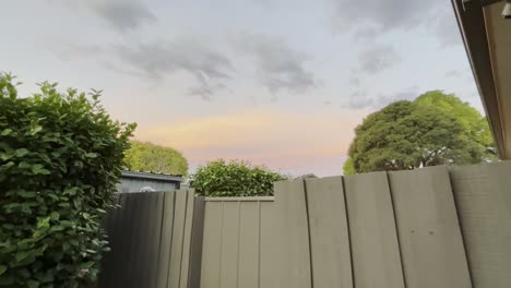 tilting shot of a gate and wood fence revealing a colourful sky with clouds at sunset.