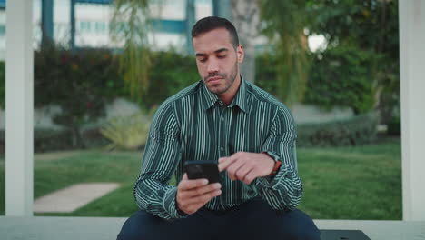 young man checking smartphone sitting in bench outdoors.