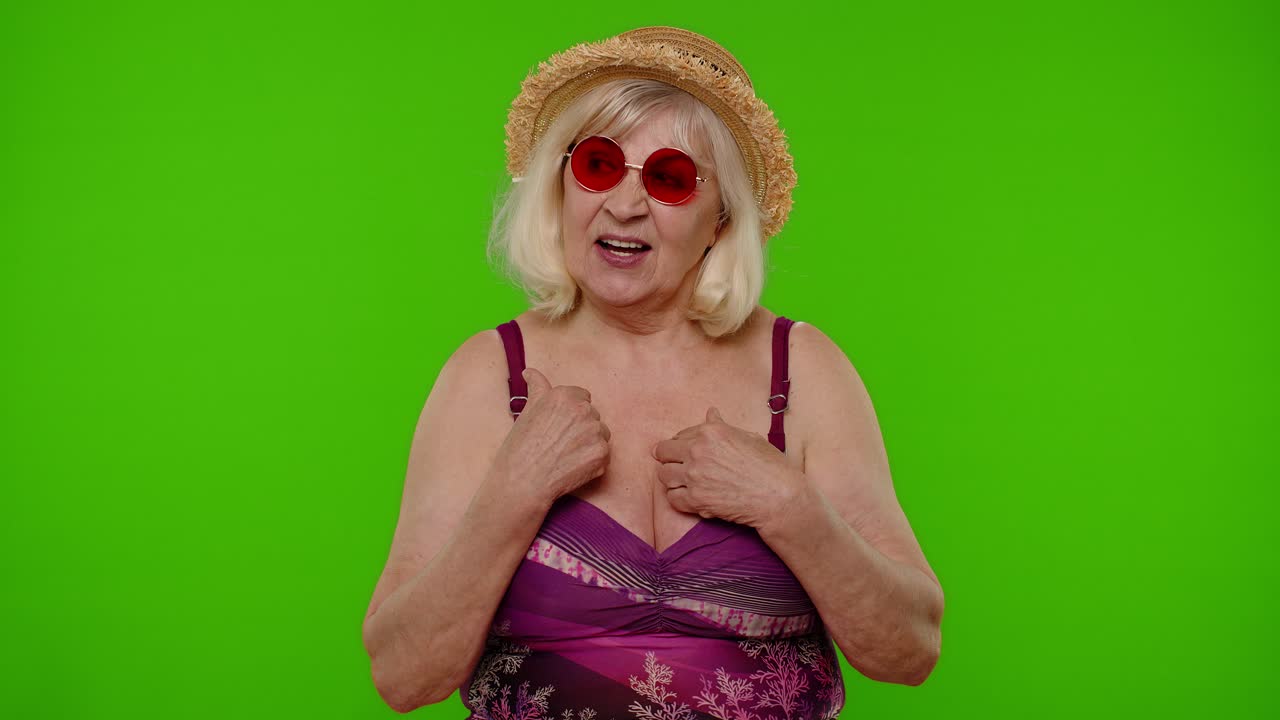 mujer madura viajera señalándose a sí misma, sonriendo satisfecha, satisfecha de su propia belleza y logros