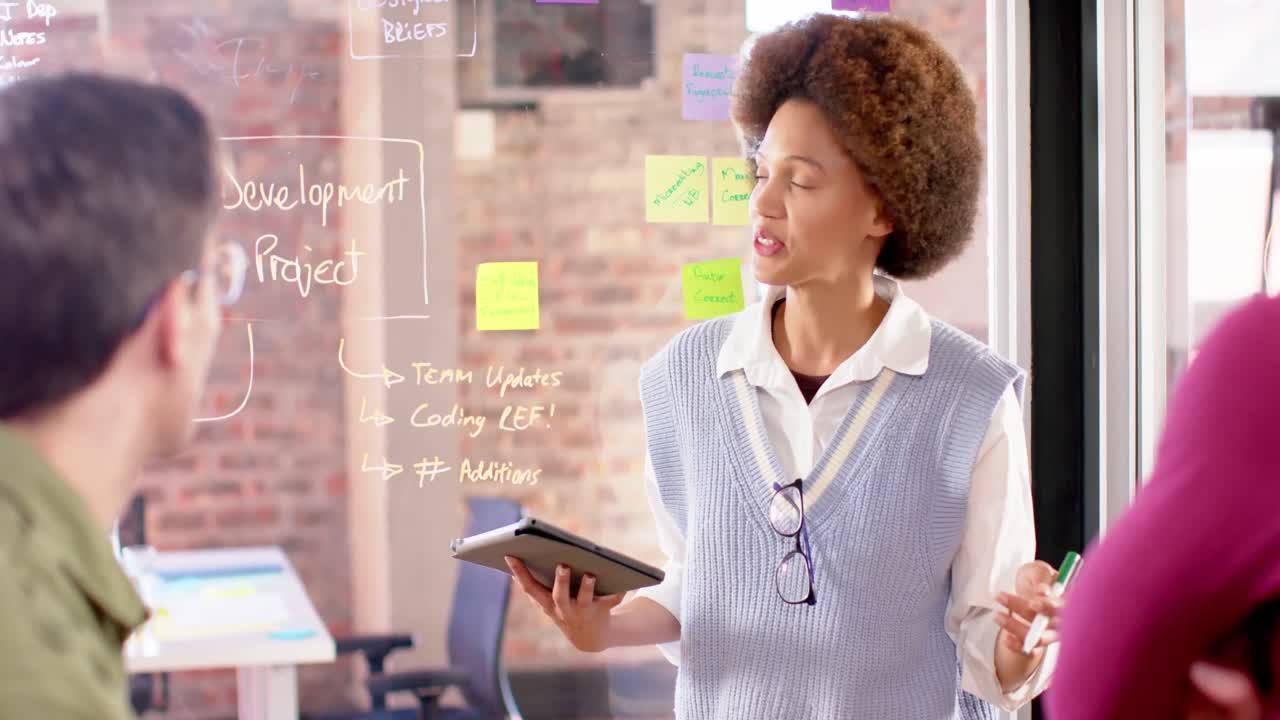 Biracial creative businesswoman with tablet in casual meeting with diverse colleagues, slow motion