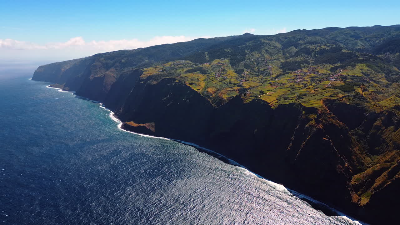 Dangerous steep cliffs at the shore of the Atlantic Ocean. Village in the green picturesque valley on the slope of the mountain in the Madeira Islands, Portugal. Top view.