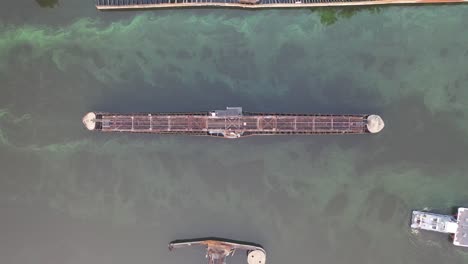 aerial view of a bridge, barge, and tugboat in a waterway with algae