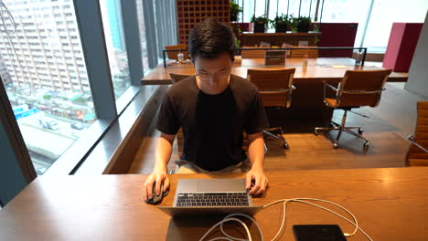chinese asian millennial walking and sitting in front of laptop to work in co-working space in hong kong. view of city traffic in background. fixed wide high angle shot