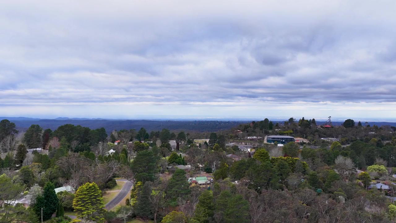 Drone che effettua una panoramica su una boscaglia di eucalipti autoctoni verso una cittadina montana periferica sotto un cielo nuvoloso