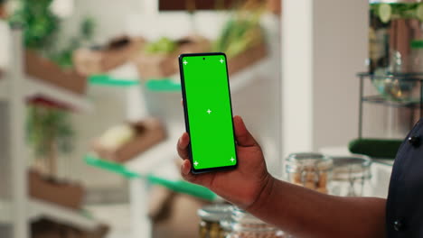 Vendor-showing-phone-with-greenscreen-layout-at-supermarket