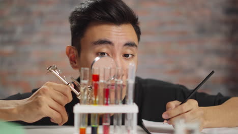 asian chemist looks at test tubes through magnifying glass