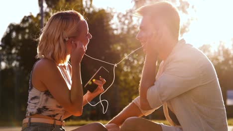 Vacaciones-De-Verano,-Tecnología-Y-Concepto-De-Personas-Pareja-Feliz-Con-Teléfonos-Inteligentes-Y-Auriculares-Escuchando-Música-Y-Besándose-Al-Aire-Libre