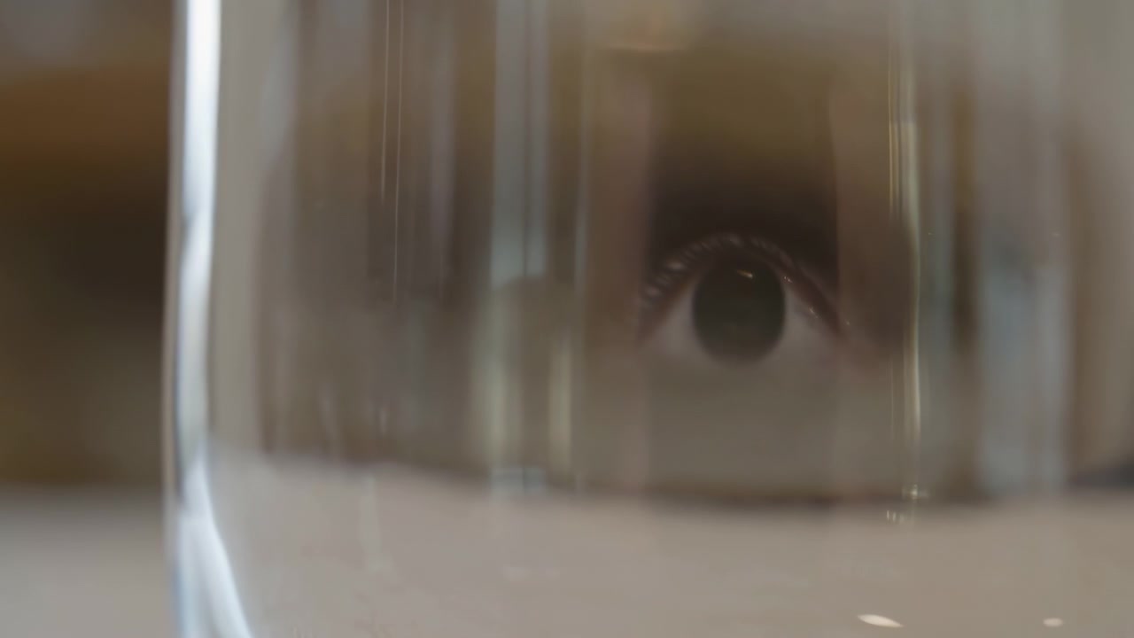 Close-up motion scene of curved transparent glass with thin vertical condensation trails lengthening along inner wall while small specular highlights reflect ceiling lights and soften details
