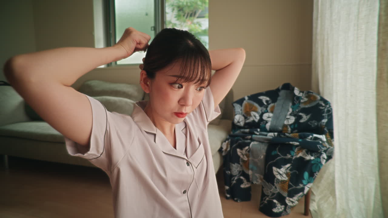 Woman tying her hair up indoors with kimono in the background