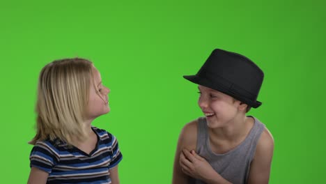 child whispers a joke to another child in front of greenscreen