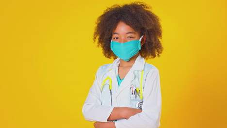 studio portrait of boy dressed as doctor or surgeon wearing face mask against yellow background