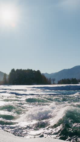 snowy river scene with splashing waves and mountains in the background under clear blue sky