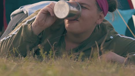 young woman with hangover drinks water lying on brown meadow