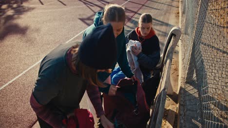 un trío de chicas con ropa deportiva ponen sus cosas en una mochila en un campo deportivo callejero después de jugar al baloncesto en una soleada mañana de verano. tres chicas rubias con uniformes deportivos de verano recogen sus cosas después de jugar a baloncesto