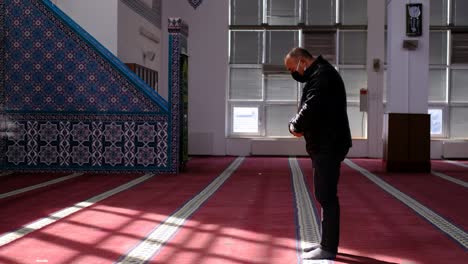 man stands and prays in mask  in a mosque