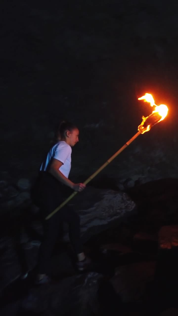 Young woman holding a flaming torch while carefully climbing over rocks inside a dark cavern in Guincho cave, Arucas, Gran Canaria island