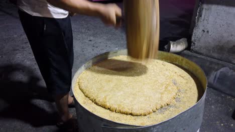 Man-hitting-hard-with-big-wooden-hammers-to-crack-grain-which-will-be-used-in-making-of-sweet-snack-for-sale-on-the-street,-China