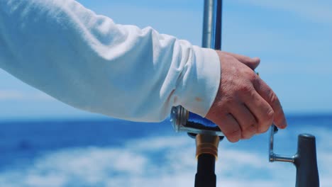 man resting hand on spinning fishing reel at sea, close up