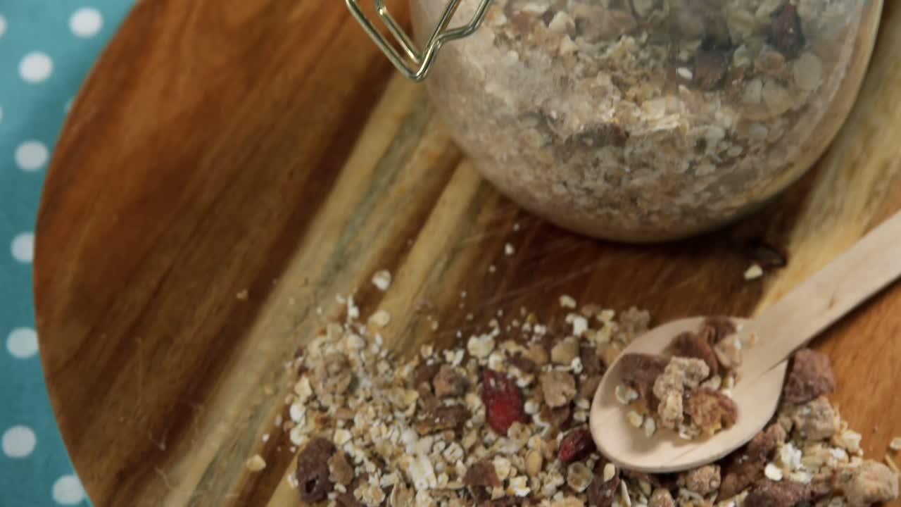 Glass jar of homemade granola and muesli with spoon on wooden board 4k