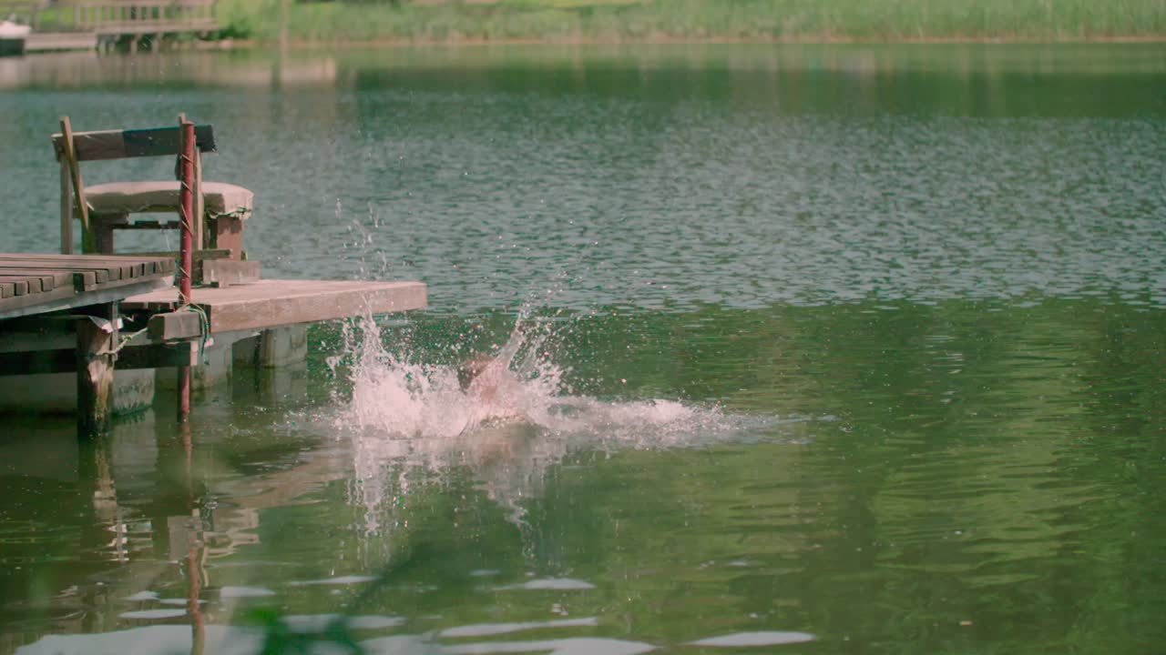 수영복을 입은 어린 소년이 목재 부두에서 물 속으로 뛰어든다