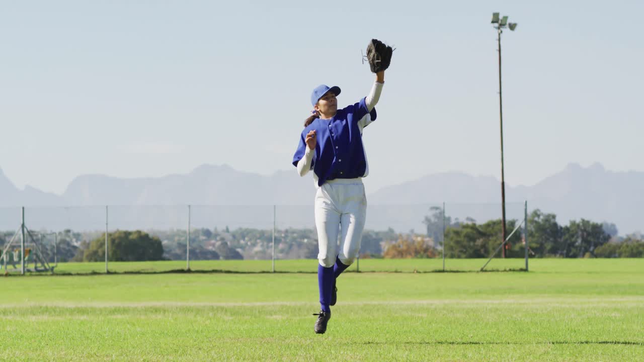 Giocatrice di baseball caucasica in difesa, che salta, afferra e lancia la palla sul campo da baseball
