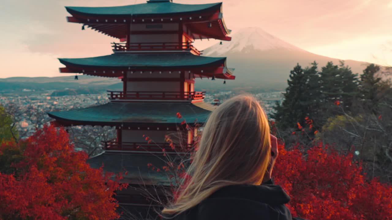 una mujer captura la impresionante vista de la pagoda chureito al atardecer, con el monte fuji en el fondo.