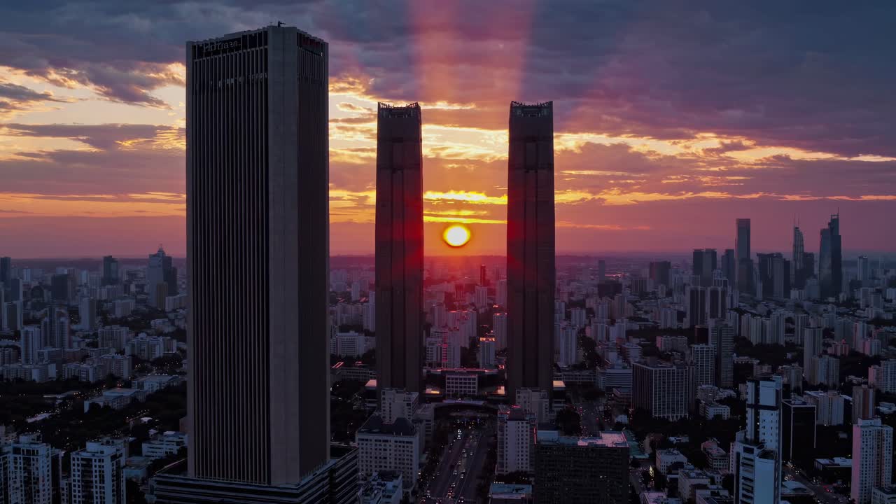 Um vídeo aéreo captura uma paisagem urbana ao pôr do sol, com arranha-céus em silhueta contra um céu vibrante