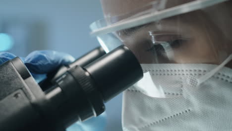 Female-Lab-Scientist-in-Protective-Uniform-Looking-through-Microscope