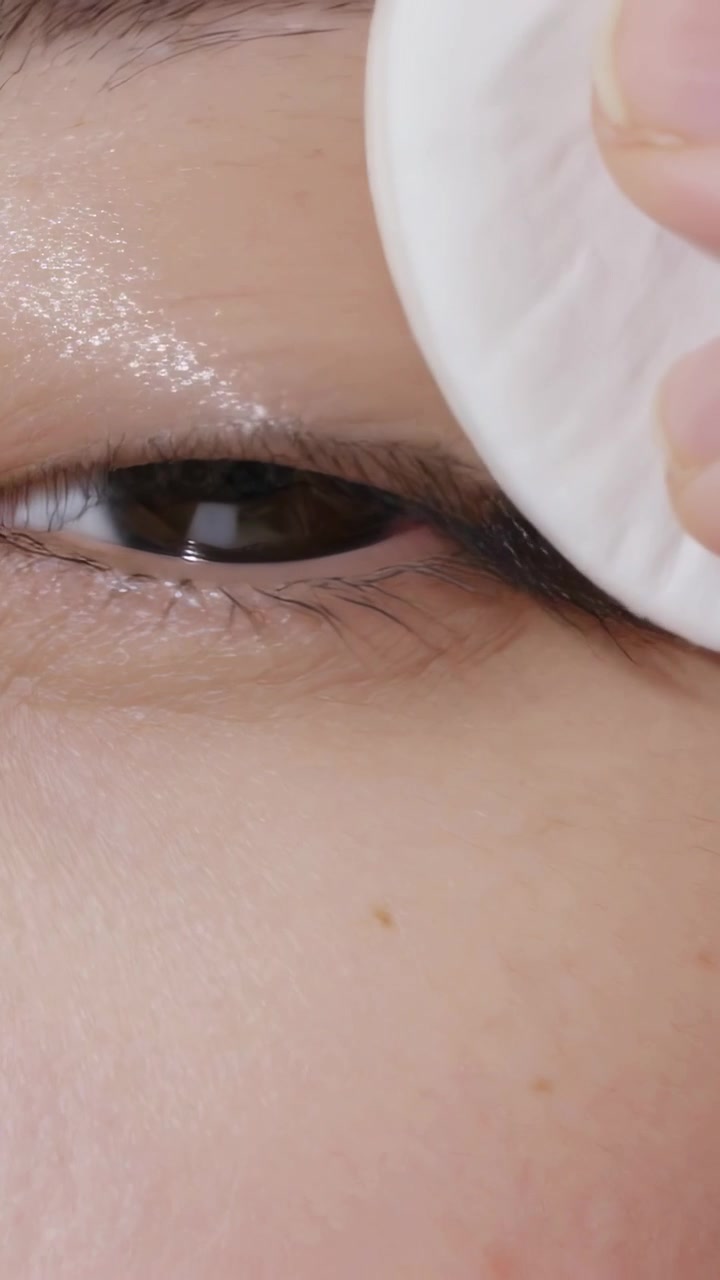 Vertical video: Pressing cotton pad with fingertip, wiping right eye at vanity, removing shimmer