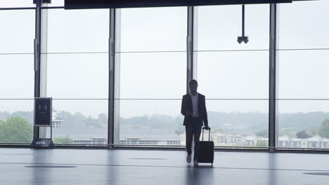 Businessman-Walking-Across-Concourse-At-Railway-Station-With-Mobile-Phone-Wearing-PPE-Face-Mask