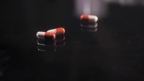 Pills-rolling-on-a-black-glass-surface,-mirror-surface-with-a-reflection-on-black-background