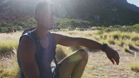 african american man exercising outdoors hiking resting on a rock in countryside on a mountain