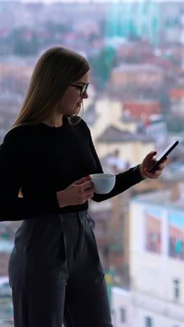 young caucasian woman wearing glasses while talking by phone and drinking coffee. coworking concept. vertical video