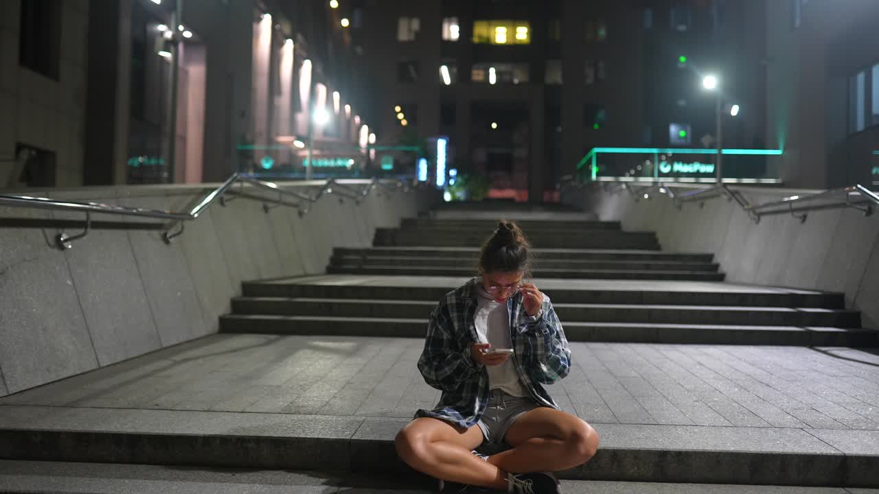 joven usando el teléfono en las escaleras de la ciudad por la noche