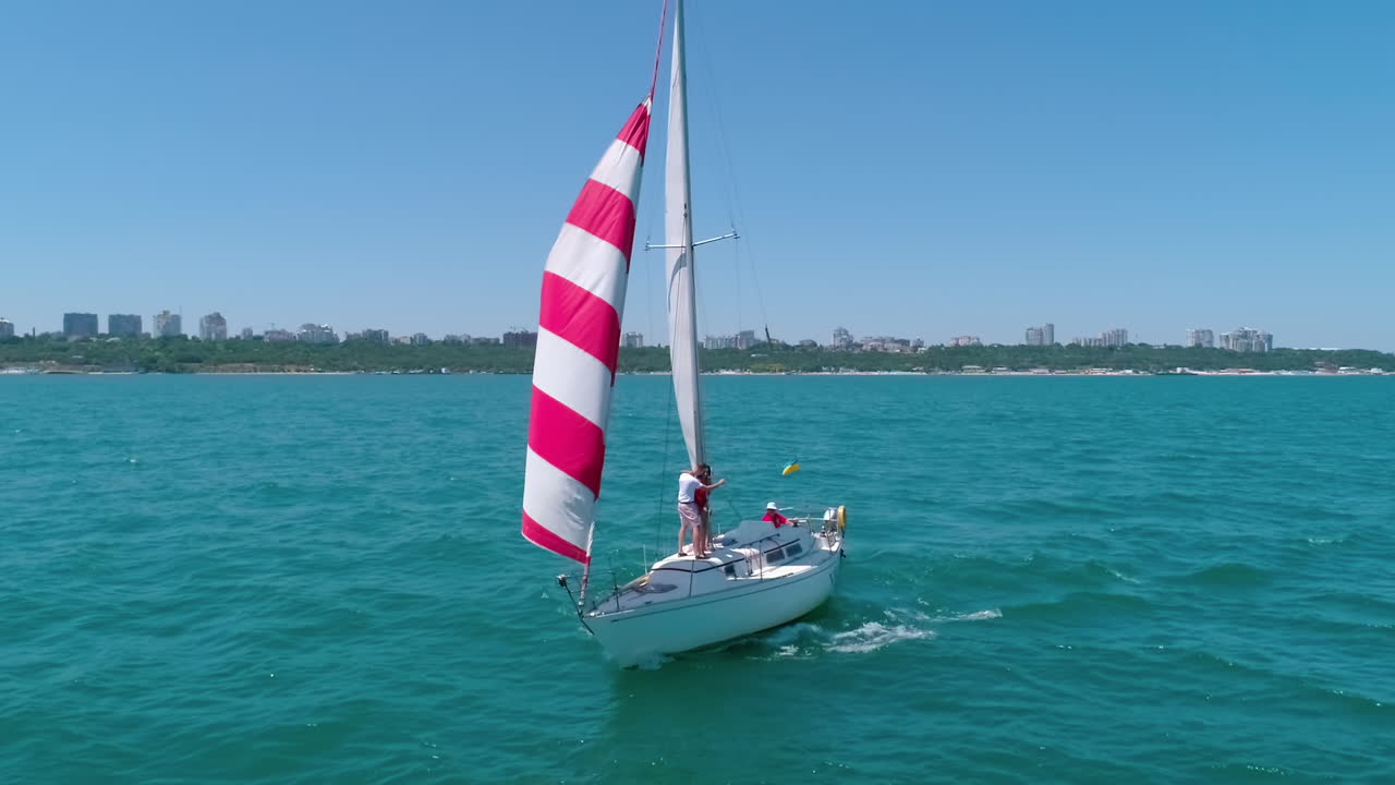 Yacht sailing on sea. Red and white sails on a boat at windy day. Sun shine over sail boat at ocean bay. Sailboat cruise on a beautiful seascape. Ship in summer sunny day.
