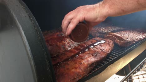 Racks-of-ribs-having-sauce-applied-in-an-off-set-smoker