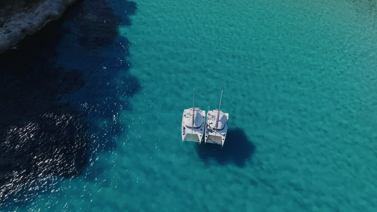 las sombras de dos yates de vela se pueden ver mientras flotan en aguas cristalinas frente a la costa de menorca.