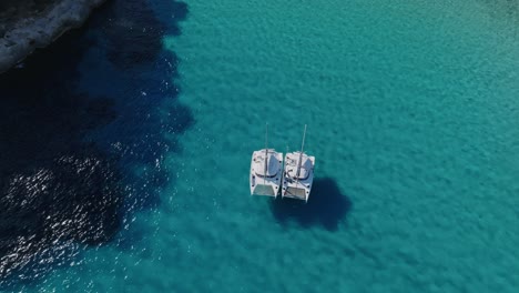 Shadows-of-2-sailing-yachts-can-be-seen-as-they-float-in-crystal-clear-waters-off-the-coastline-in-Menorca