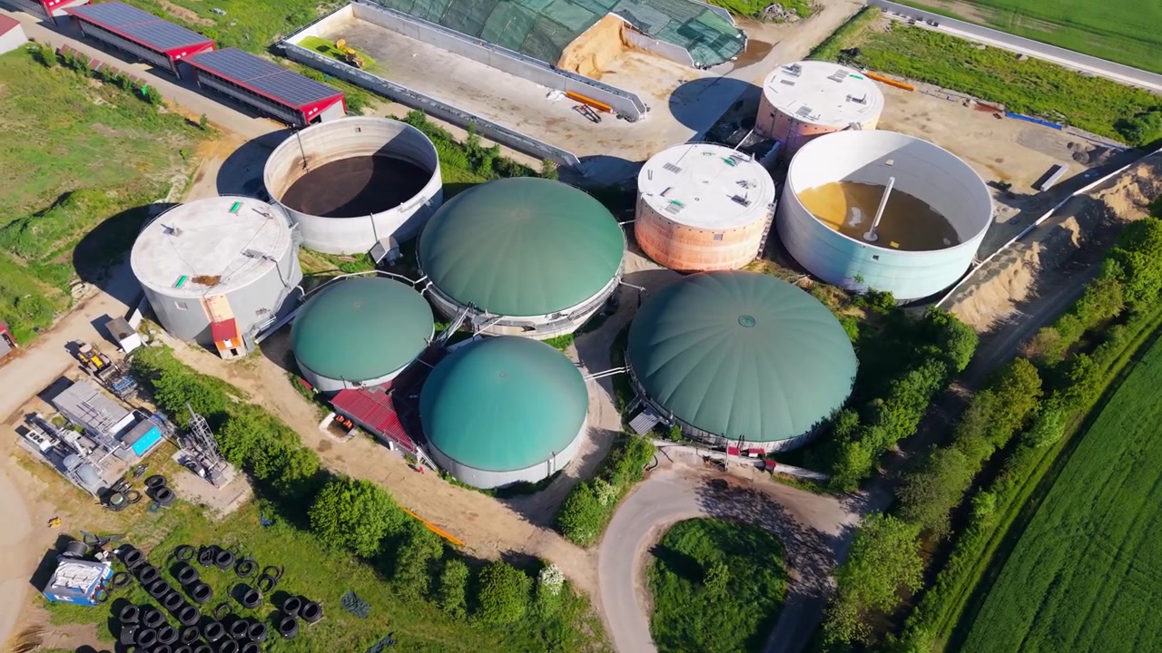 Imagem de mapeamento de drone em ângulo elevado de uma instalação de bioenergia apresentando múltiplos domos de fermentação, silos de armazenamento e campos circundantes na Baviera
