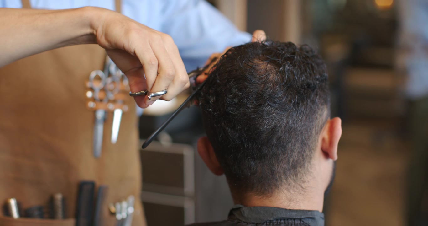 Barber, der løfter hår med kam og bruger saks til at forme frisure i salonen.