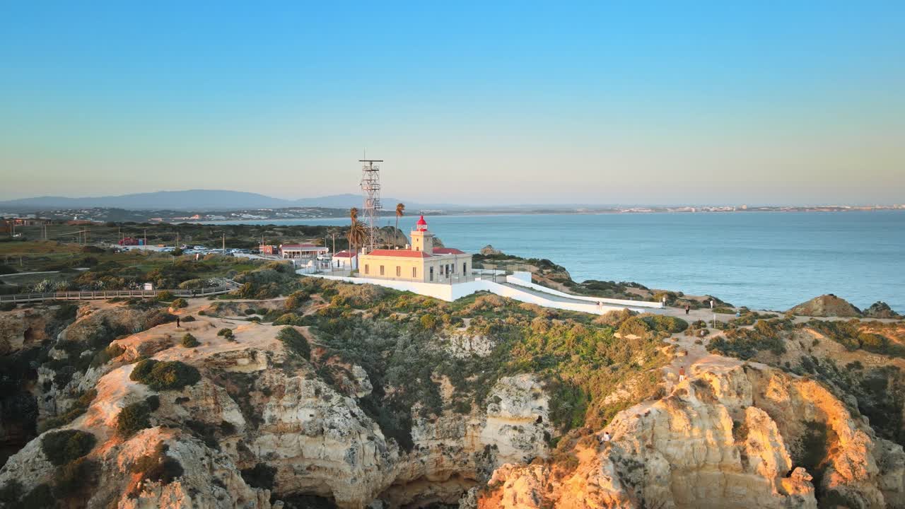 Camera spirals around Ponta da Piedade lighthouse, capturing rugged cliffs, coastal trails, and sweeping Atlantic views under the clear Algarve sky