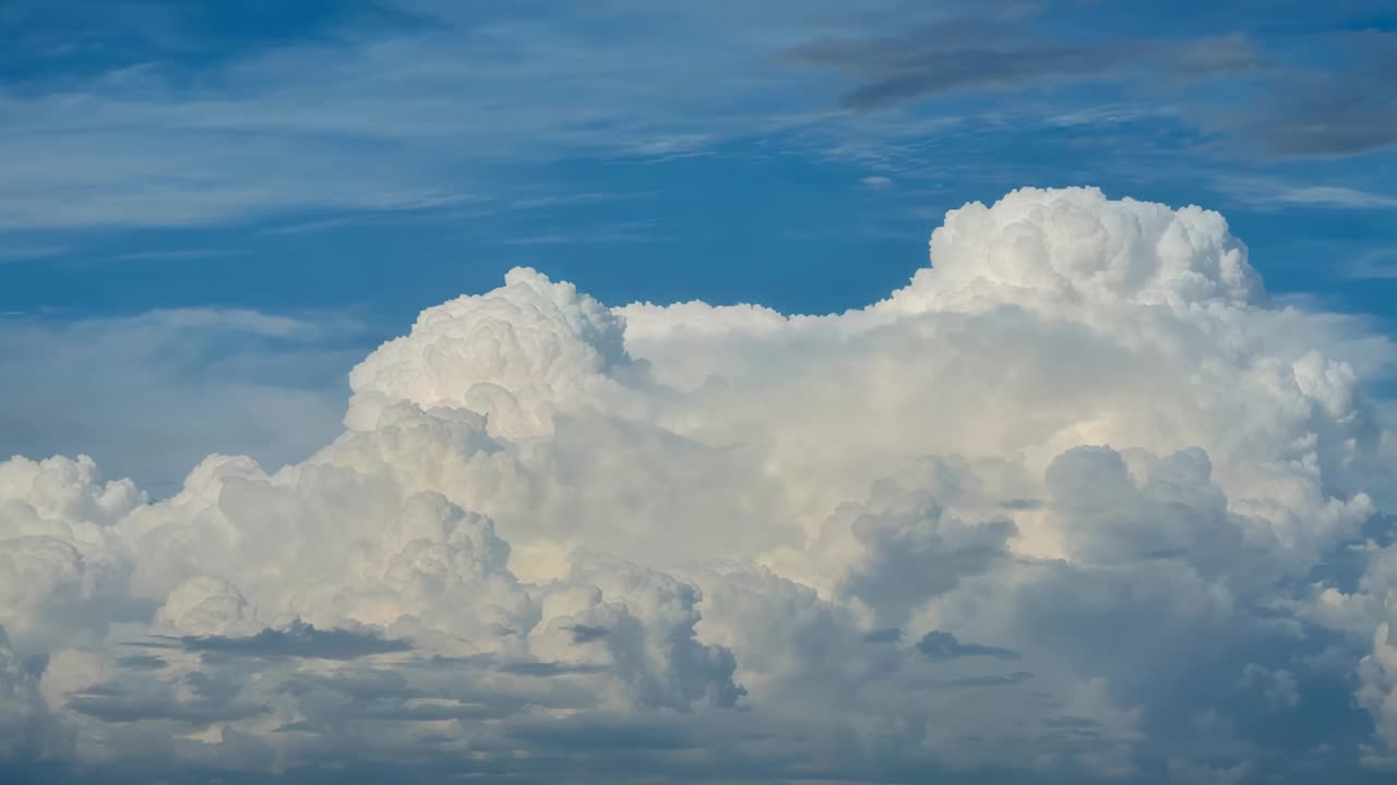 Opening showing cumulus cloud rising, expanding in deep blue sky, with anvil top and cirrus streaks