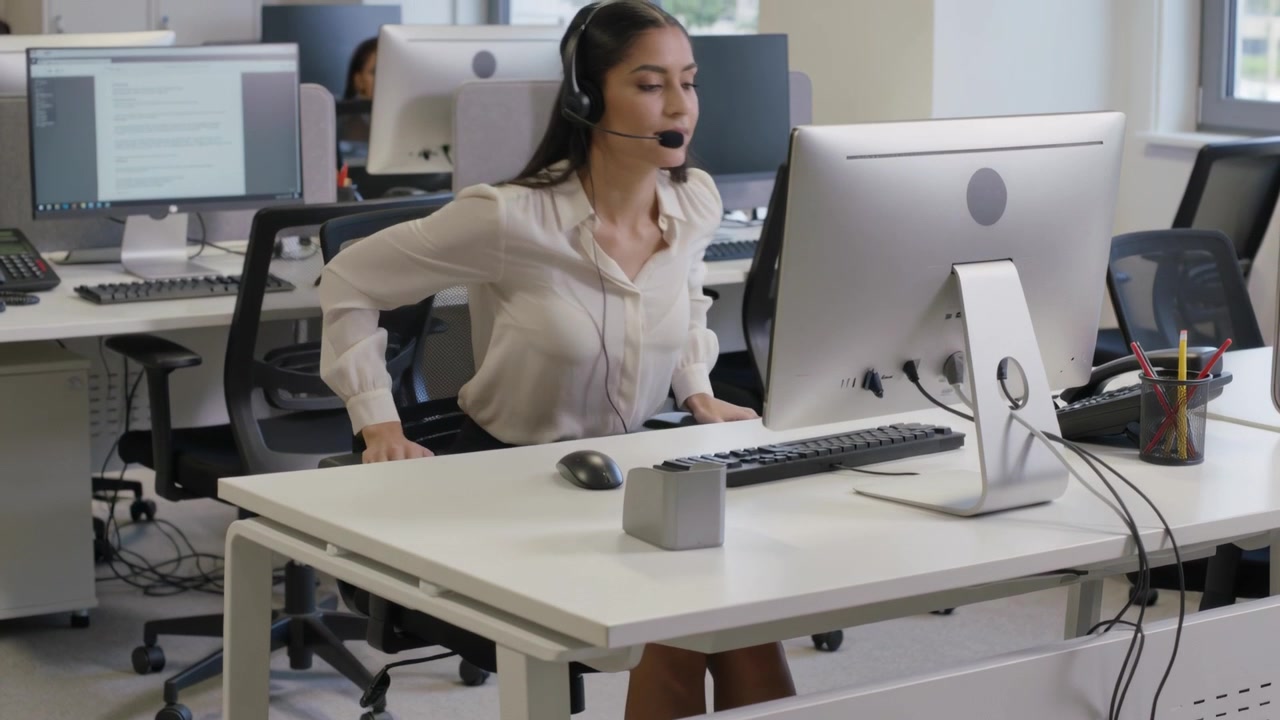Agente de call center de blusa ajustando a postura na cadeira, preparando-se para falar no headset.