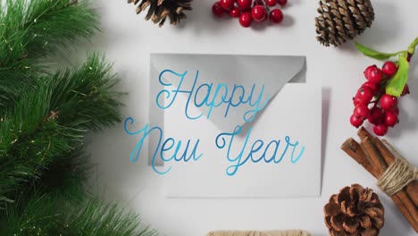 Animation-of-happy-new-year-text-banner-over-christmas-decorations-and-envelope-on-grey-surface