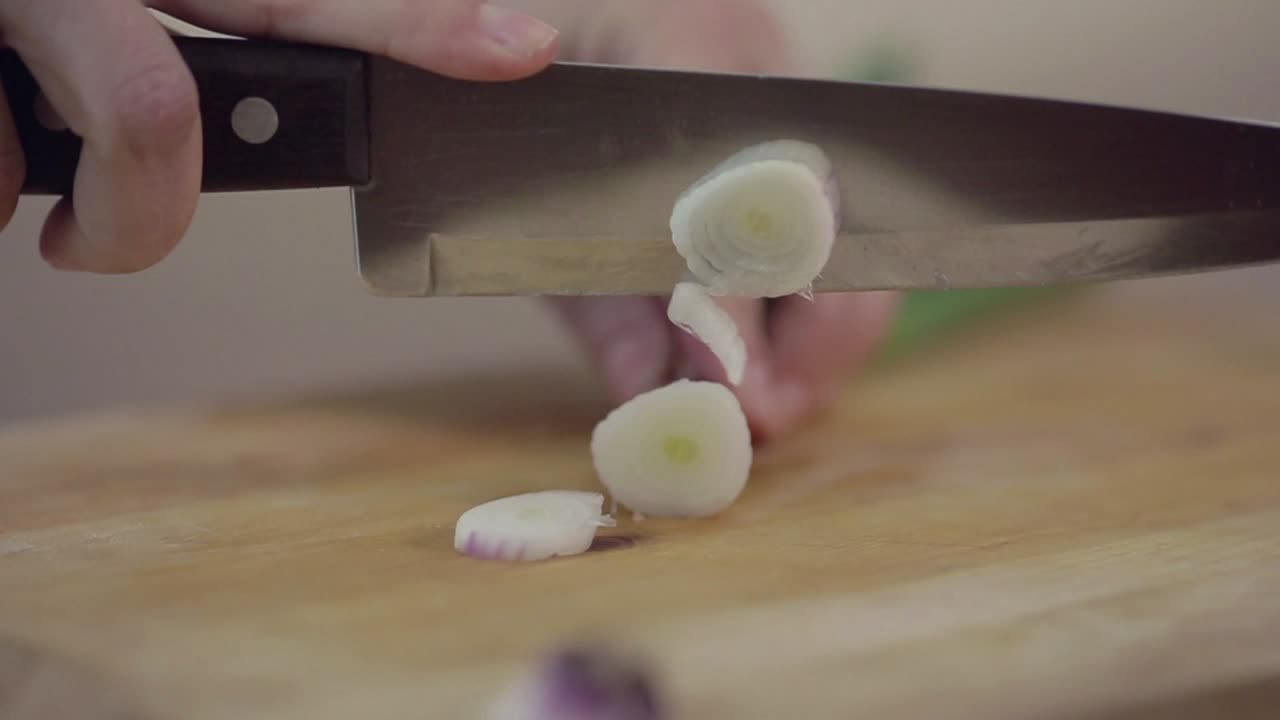 Close-Up of Hands Chopping Spring Onion on a Wooden Cutting Board